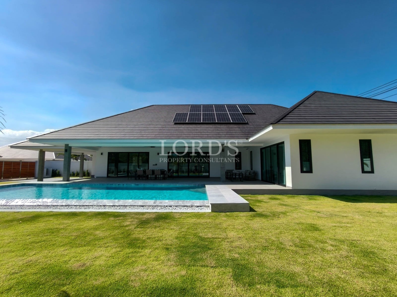 Modern pool villa exterior with private swimming pool, solar panels, covered terrace, and landscaped lawn.