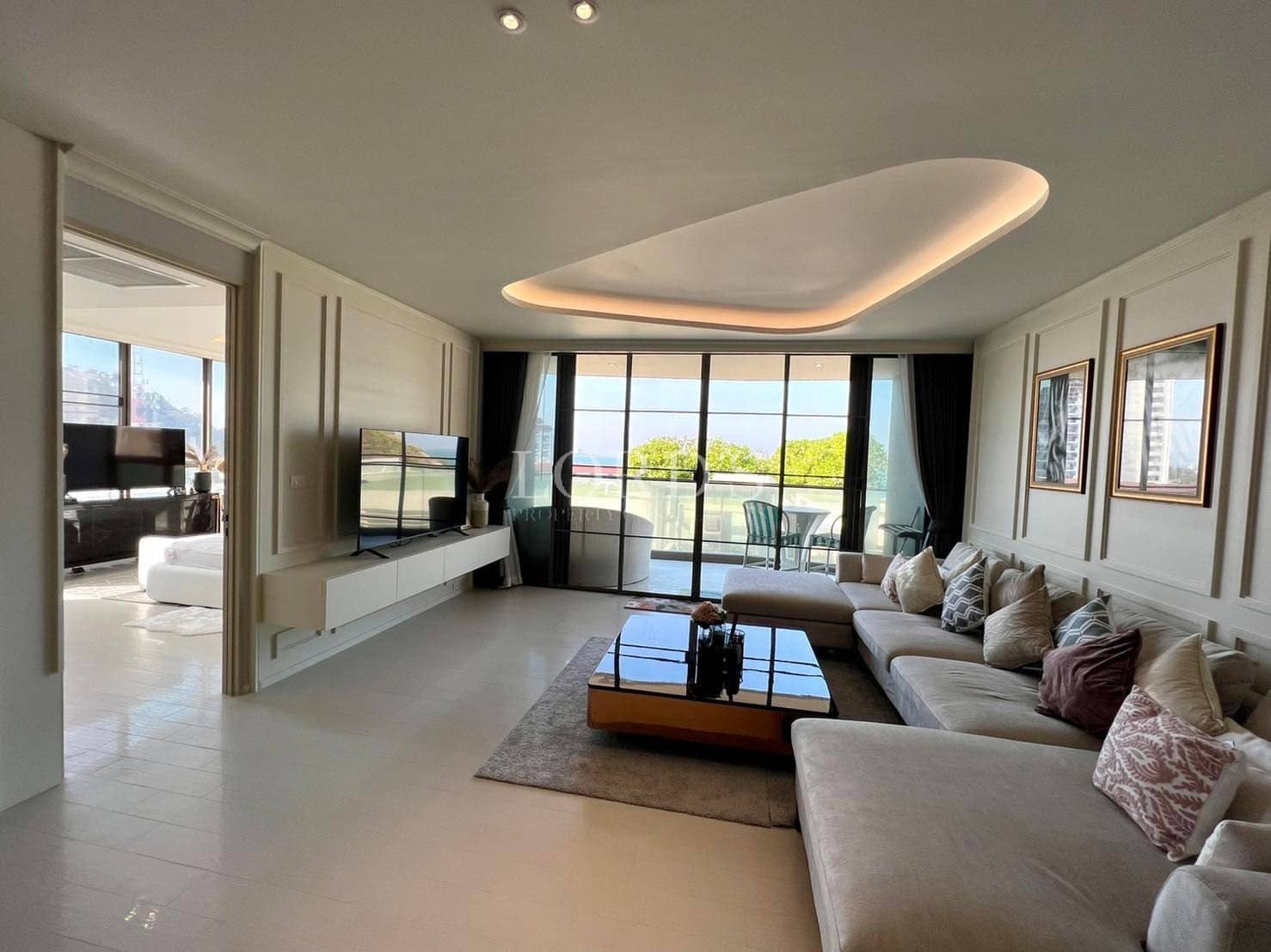 Spacious modern living room with a sectional sofa, sculptural ceiling lighting, and large glass doors opening to a balcony.