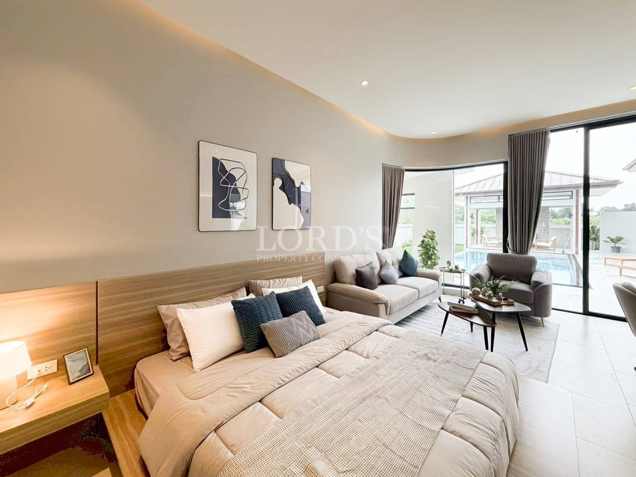 Elegant studio bedroom with a king-size bed, lounge seating area, abstract wall art, wooden accents, and large sliding glass doors opening to a private pool.