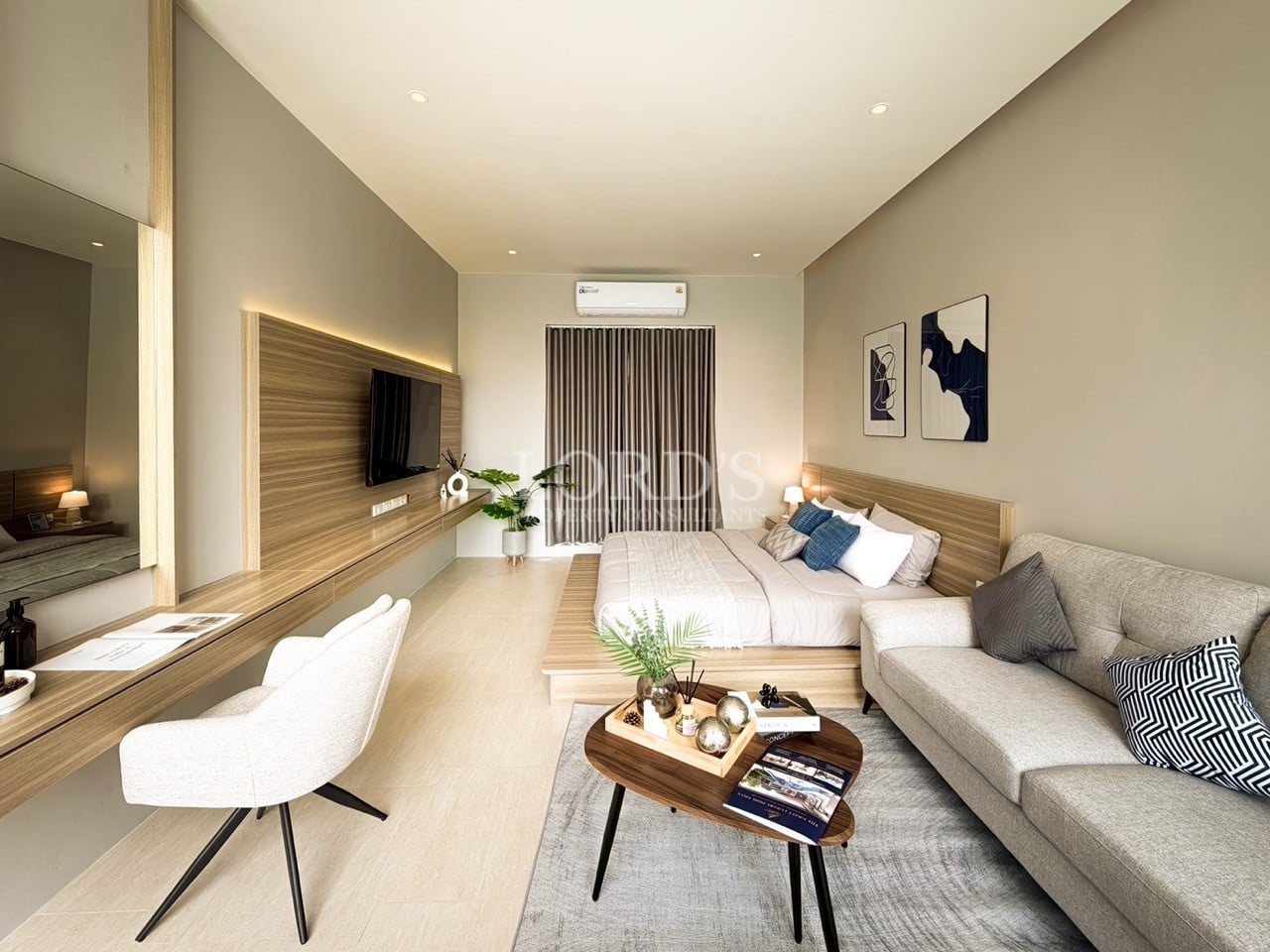 Modern studio-style bedroom with integrated living area, wooden accents, wall-mounted TV, neutral furnishings, and soft ambient lighting.