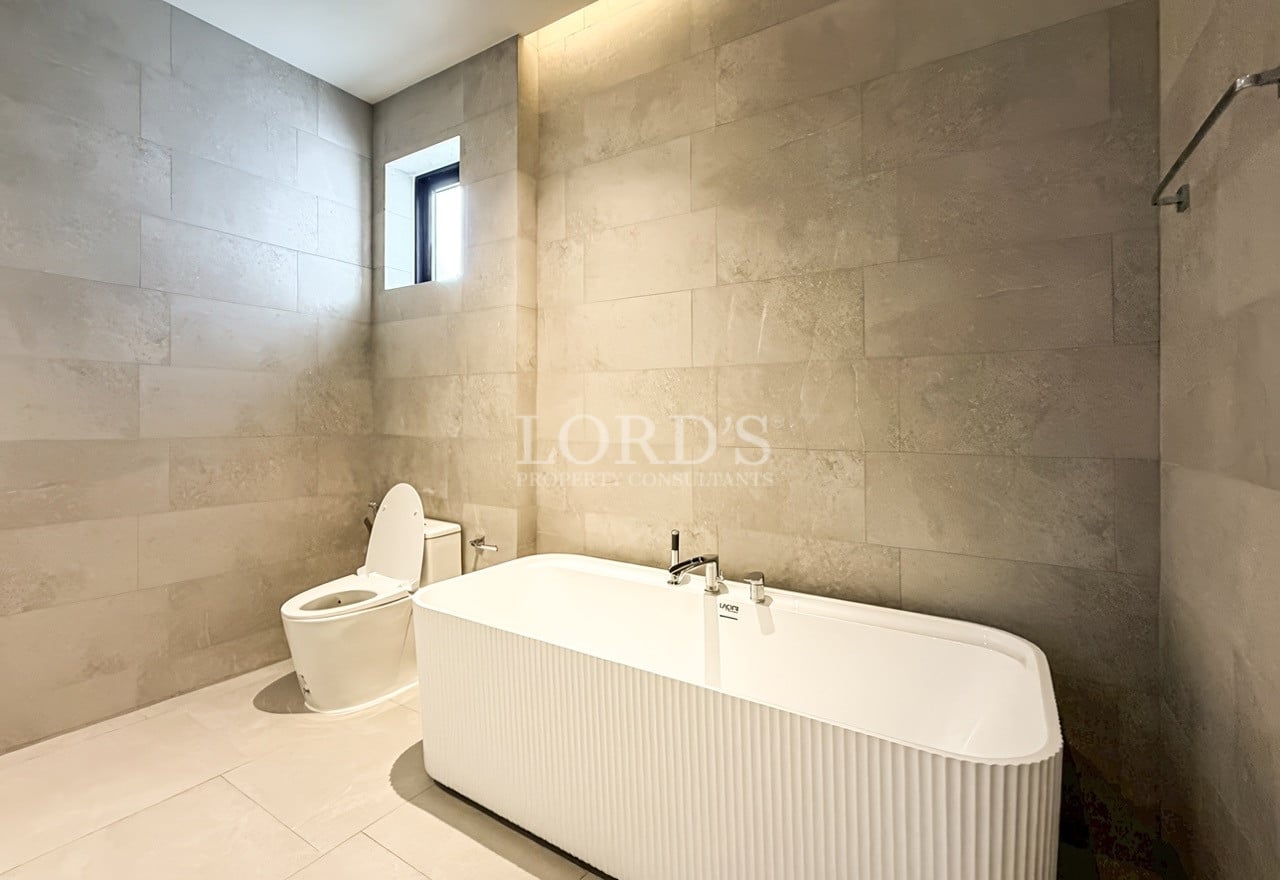 Minimalist bathroom with freestanding bathtub, stone tile walls, wall-mounted fixtures, and soft ambient lighting.