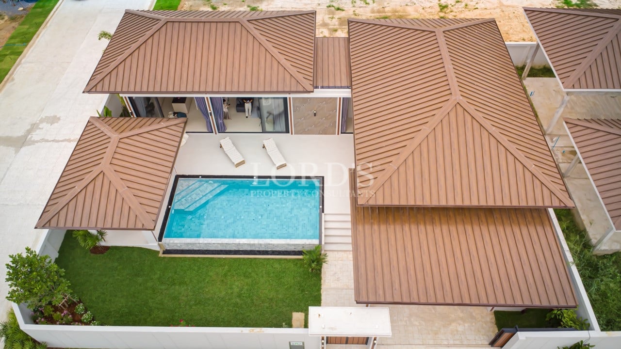 Aerial view of a modern villa with private swimming pool, landscaped garden, and multiple pitched roofs.