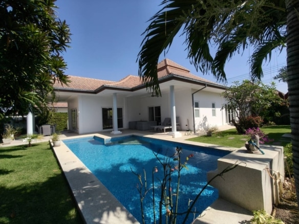 Luxury villa with private swimming pool, covered patio, white exterior, and landscaped tropical garden under a clear blue sky.