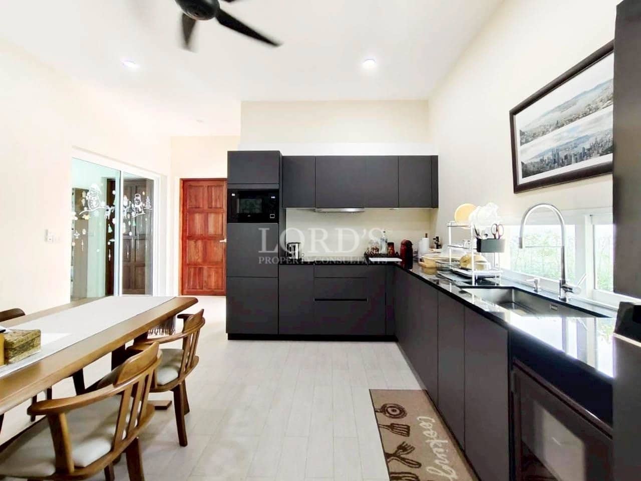 Modern open-plan kitchen with matte black cabinets, wooden dining table, and natural light.