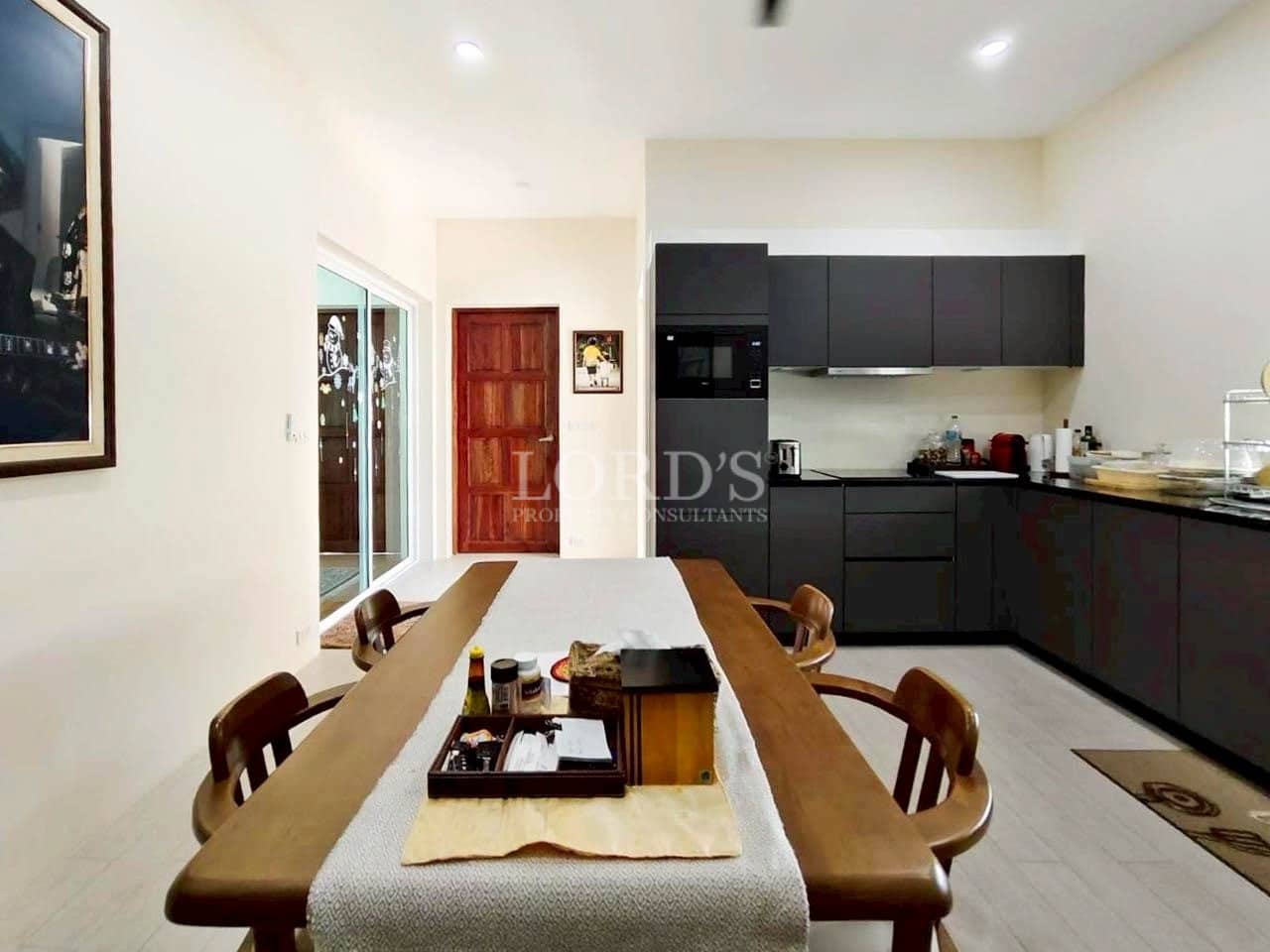 Modern dining area with wooden table, chairs, and a minimalist black kitchen in the background.