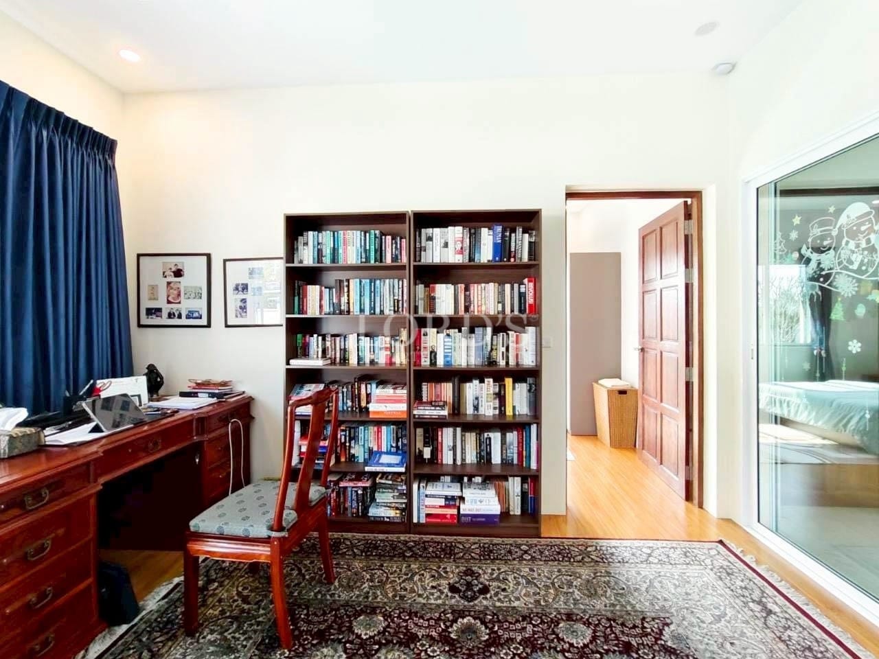 Home office with wooden desk, chair, large bookshelf, and natural light from sliding glass door.