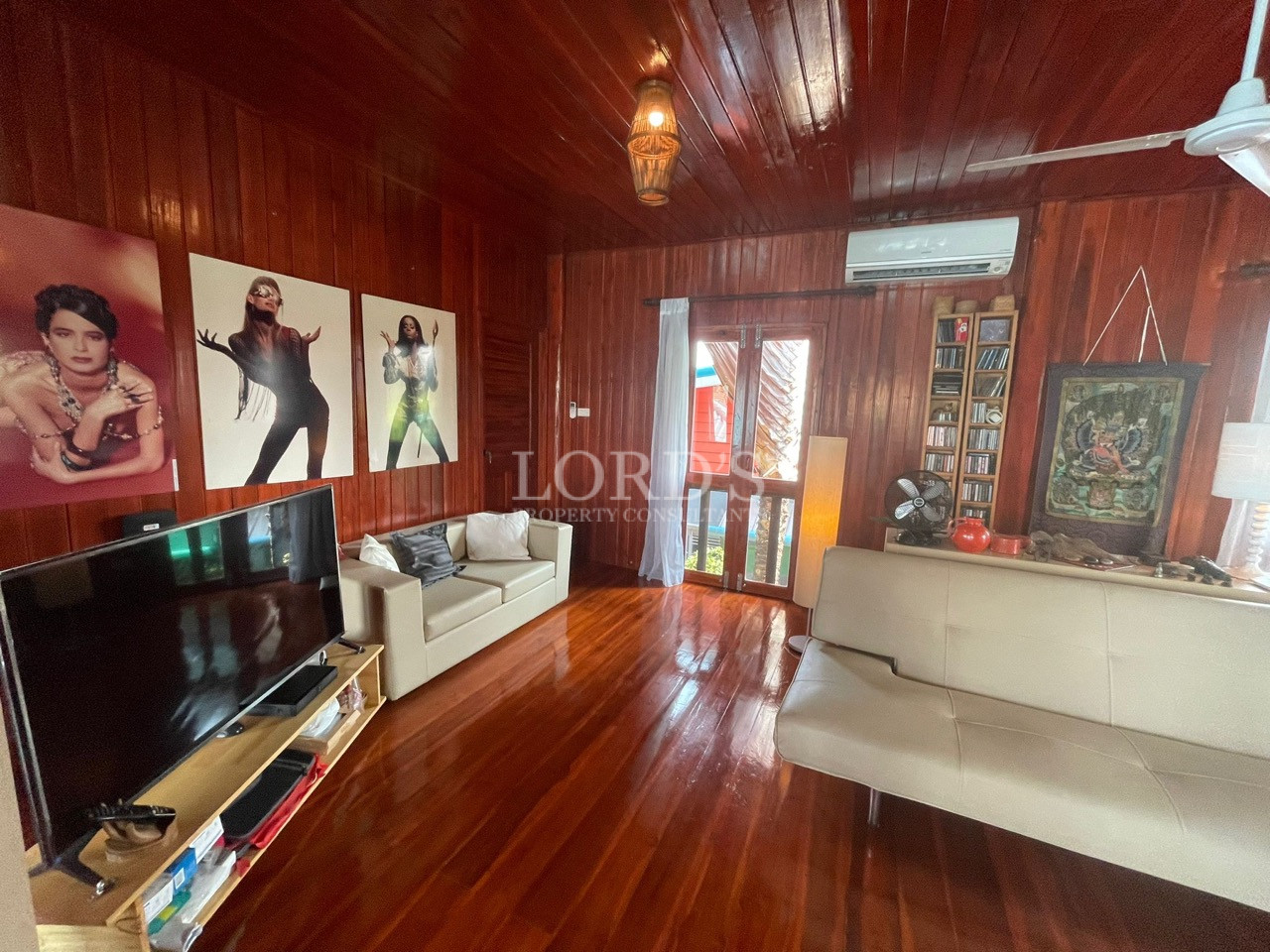 Wooden living room with polished floors, sofas, wall art, television, and natural light.
