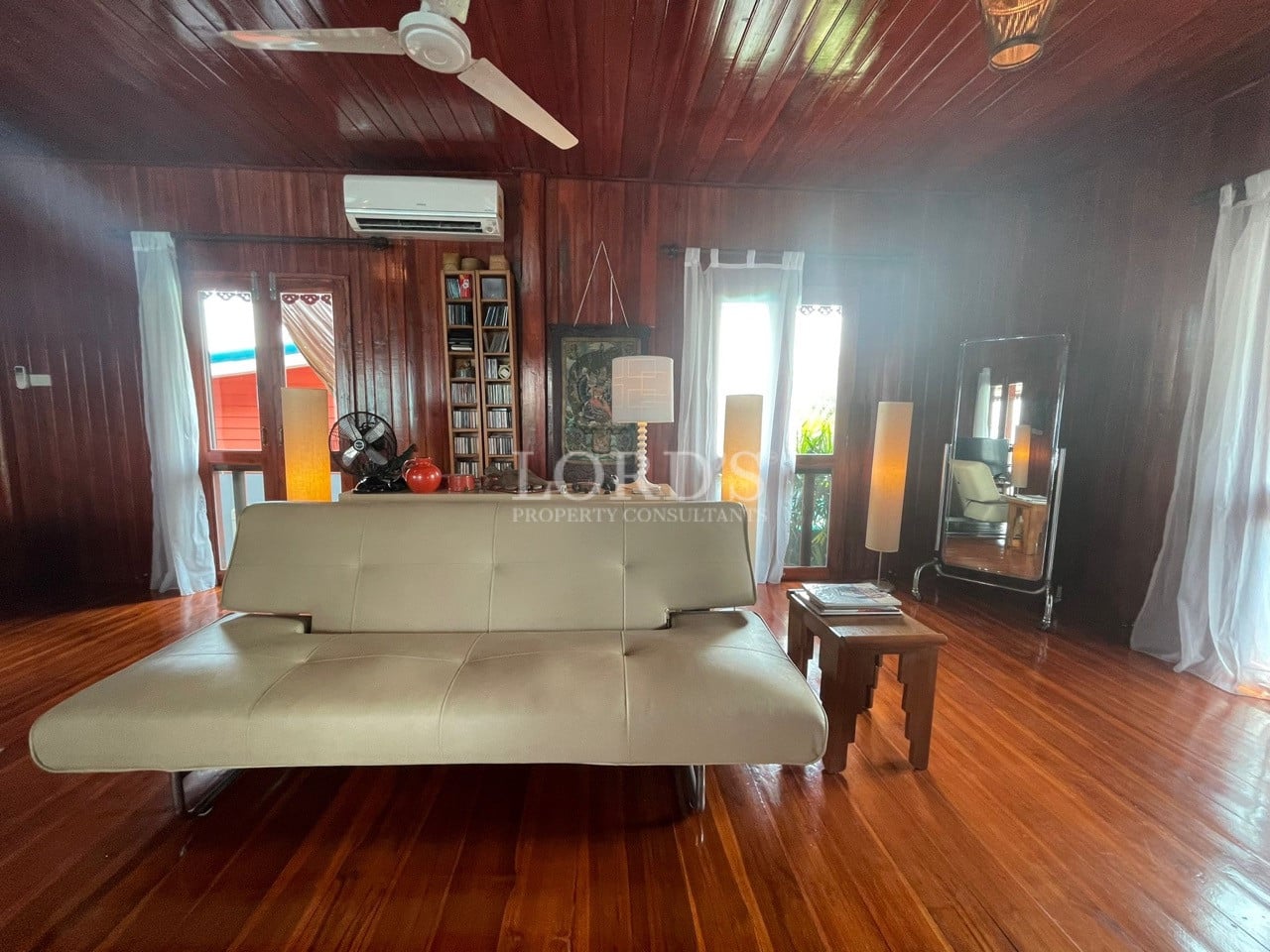Spacious wooden living room with sofa bed, polished hardwood floors, ceiling fan, and natural light.