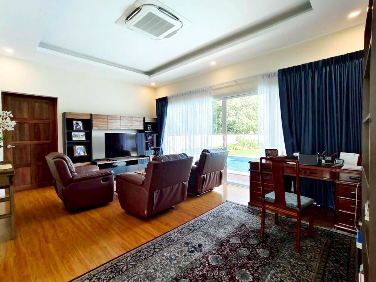 Modern home office and media room with wooden flooring, recliner chairs, TV unit, and study desk near large window.