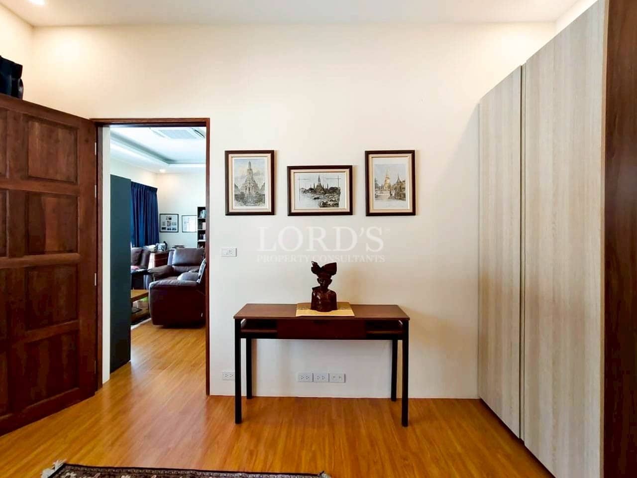 Minimalist bedroom interior with wooden flooring, wall art, study table, and built-in wardrobe.
