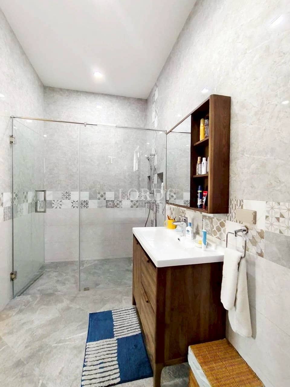 Modern bathroom with glass shower, wooden vanity, and marble tiles.