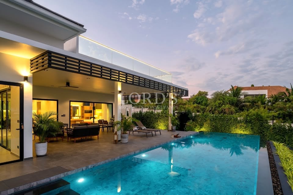 Luxury modern villa with illuminated private swimming pool, covered terrace, and landscaped garden at dusk