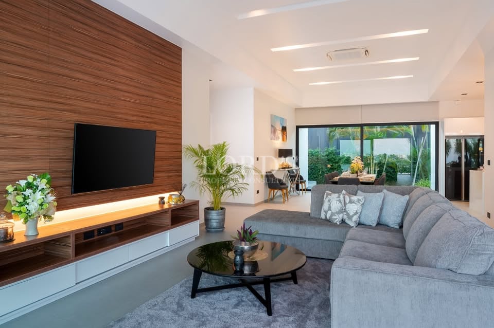 Modern open-plan living room with wood accent TV wall, grey sectional sofa, and garden view through sliding glass doors