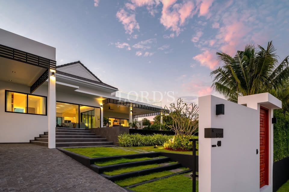 Modern luxury villa exterior at dusk with landscaped garden, illuminated interior, and contemporary entrance design