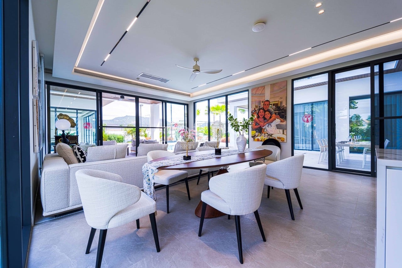 Moderner offener Ess- und Wohnbereich mit gepolsterten Stühlen, Esstisch aus Holz, Deckenventilator und großen Glasschiebetüren, die zum Außenbereich führen.