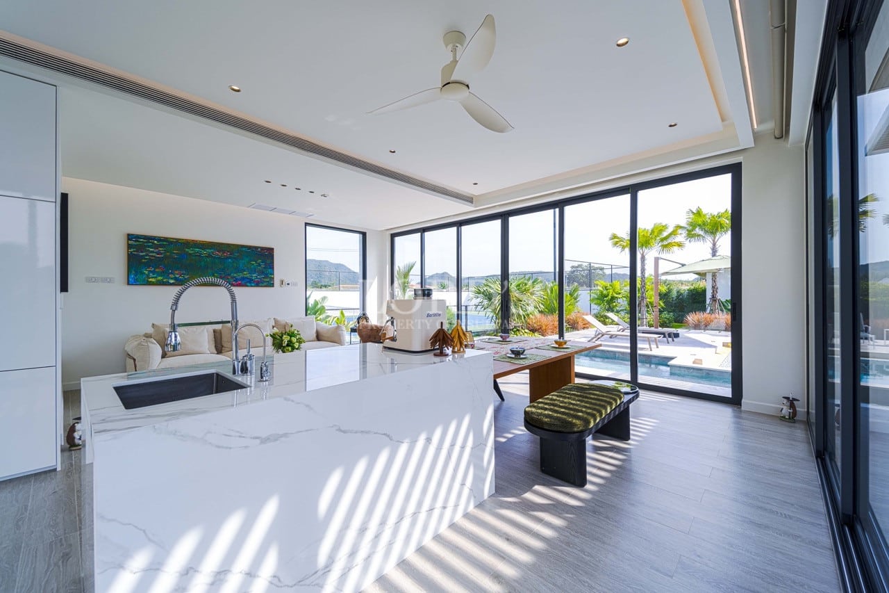 Offene Luxusküche mit Marmorinsel, Deckenventilator und raumhohen Glastüren mit Blick auf einen privaten Pool und Garten.