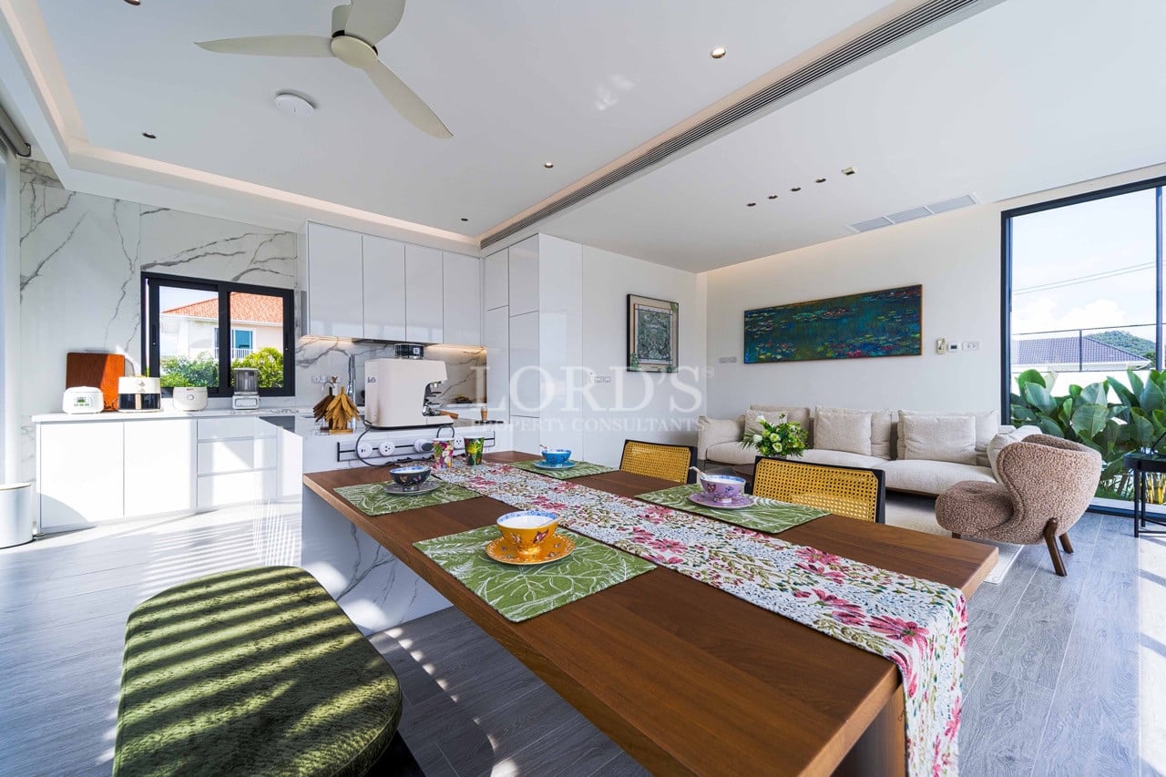 Offener Küchen- und Essbereich mit Holztisch, modernen weißen Schränken und hellen Sitzgelegenheiten im Wohnzimmer.