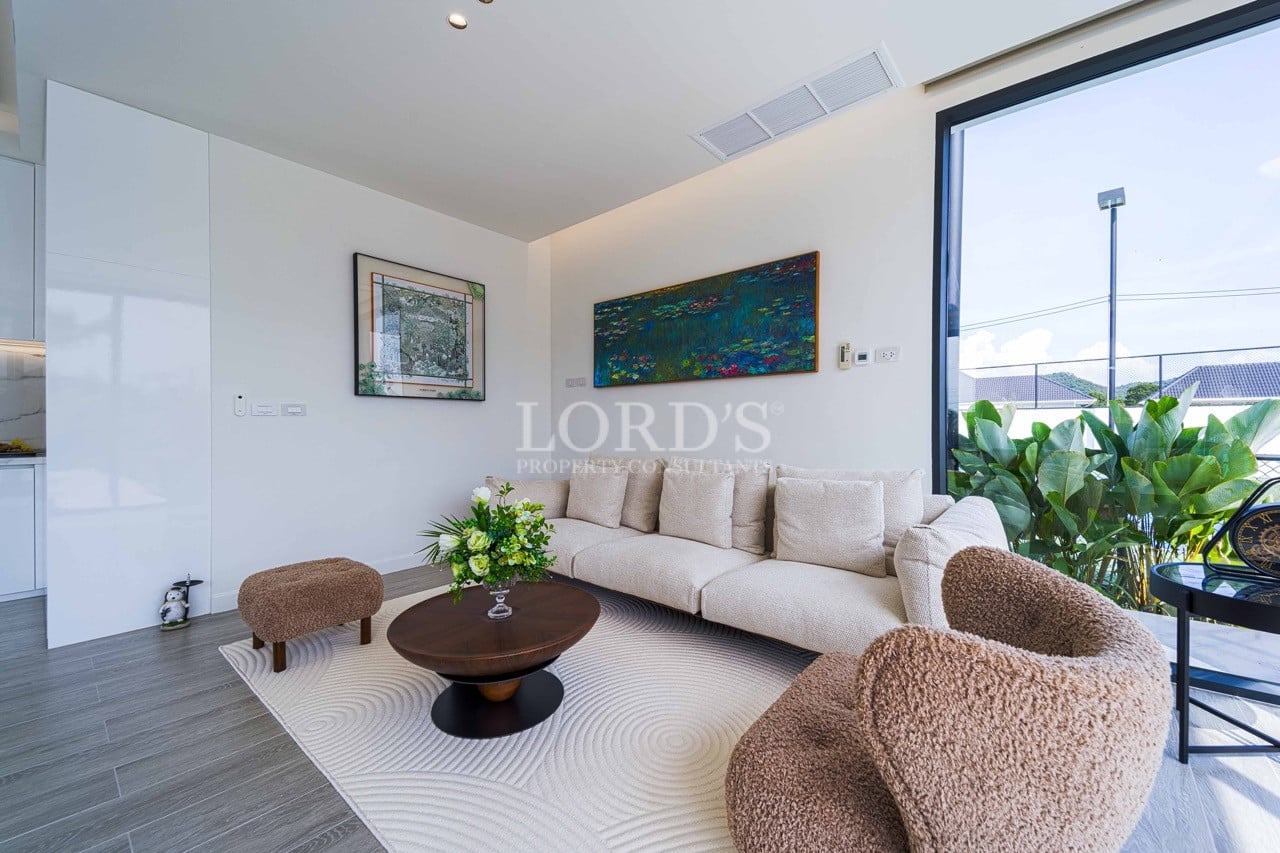 Modernes Wohnzimmer mit beigem Sofa, strukturierten Loungesesseln, rundem Couchtisch und raumhoher Glastür.