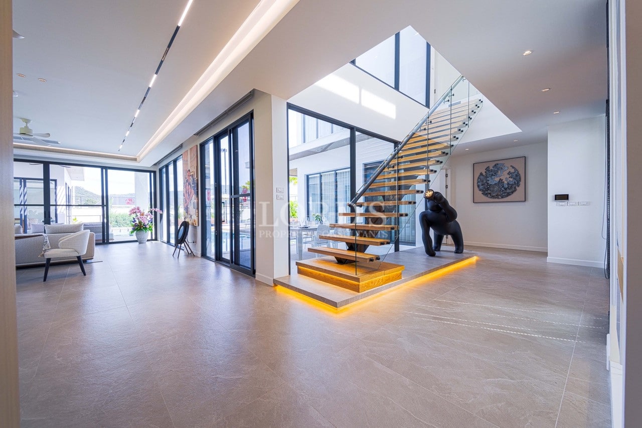 Moderner offener Wohnbereich mit schwebender Holztreppe, Glasgeländer, Oberlicht und raumhohen Fenstern.