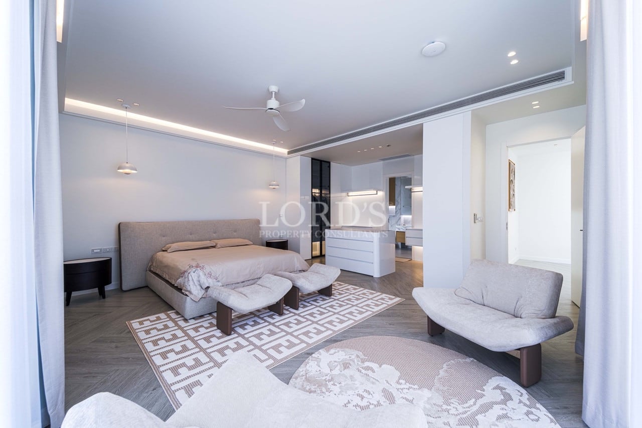 Geräumiges, modernes Schlafzimmer mit begehbarem Kleiderschrank, neutralen Farbtönen, Deckenventilator und integrierter Beleuchtung.