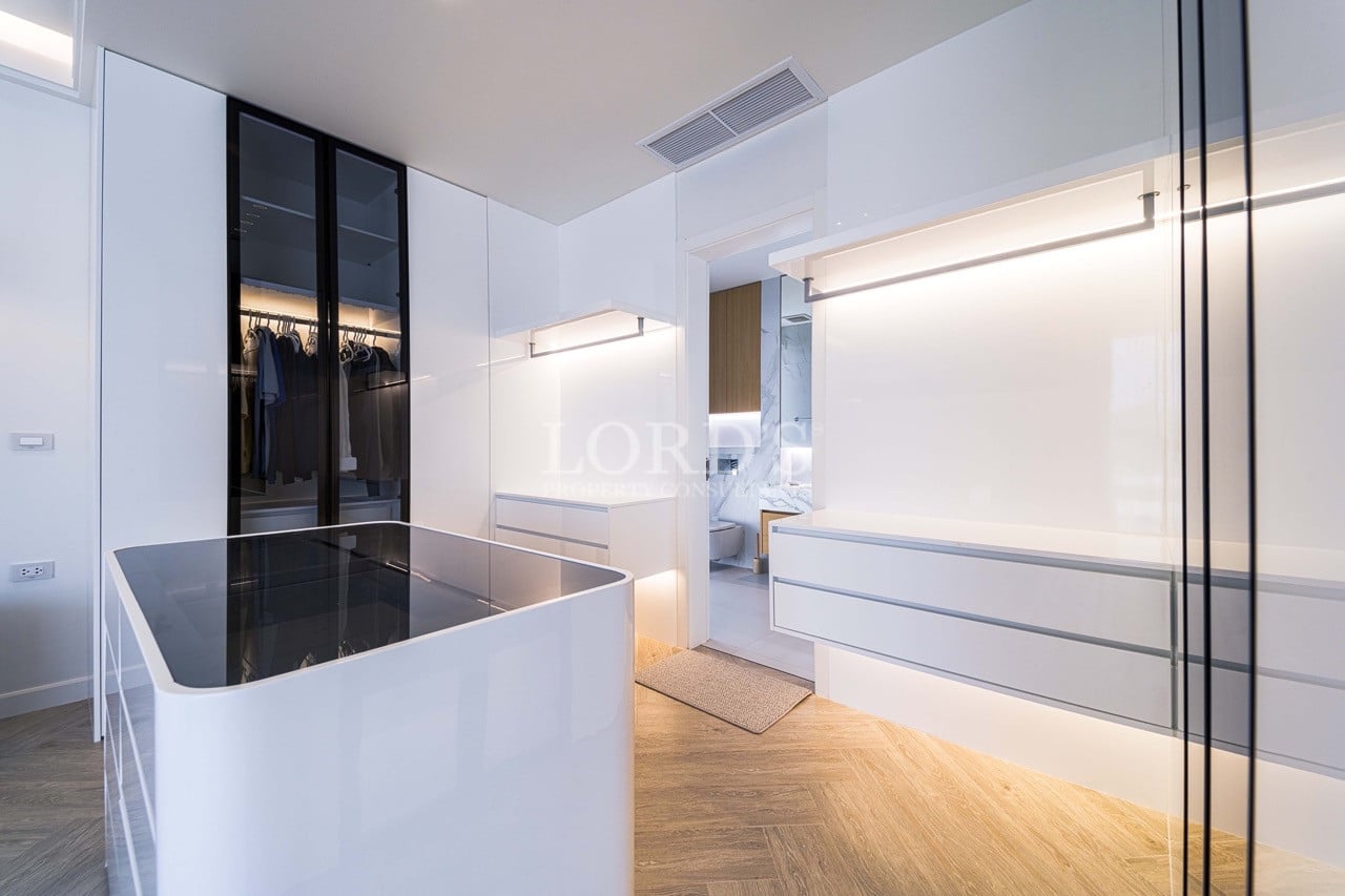 Luxuriöser begehbarer Kleiderschrank mit glänzend weißen Schränken, Glasfronten, beleuchteten Regalen und zentraler Insel.