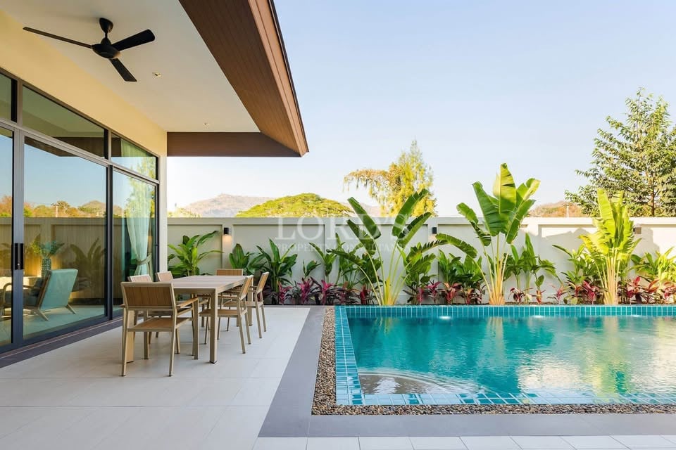 Modern villa outdoor dining area beside private swimming pool with tropical garden.