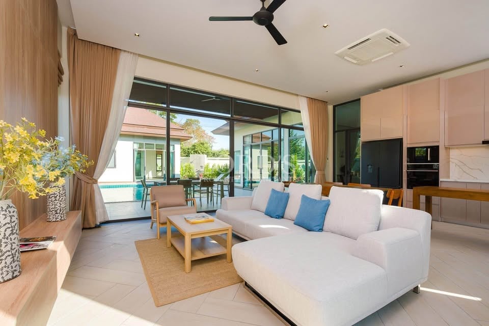 Modern open-plan living room with white sofa, glass sliding doors, and pool view.
