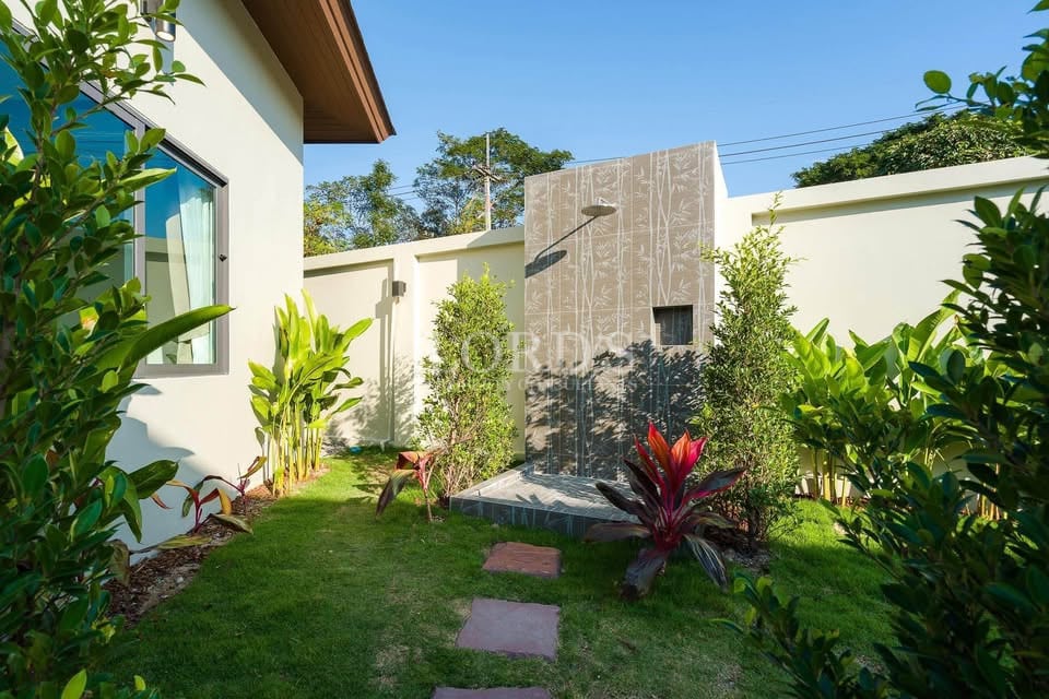 Outdoor garden shower with modern stone wall surrounded by tropical plants and greenery.