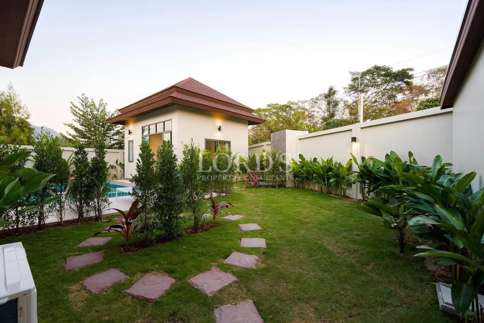 Private villa garden with landscaped lawn, stepping stone pathway, and poolside view.