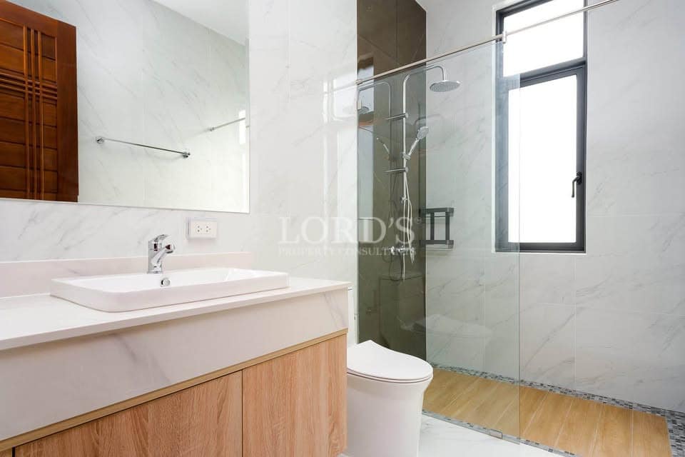 Modern bathroom with glass shower enclosure, wooden vanity, and minimalist white interior.