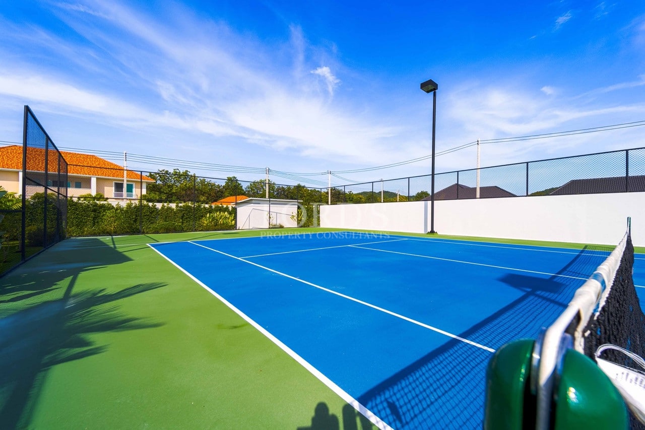 Privater Tennisplatz in voller Größe mit blauer Spielfläche, grünem Außenplatz, Umzäunung und Wohnumgebung.