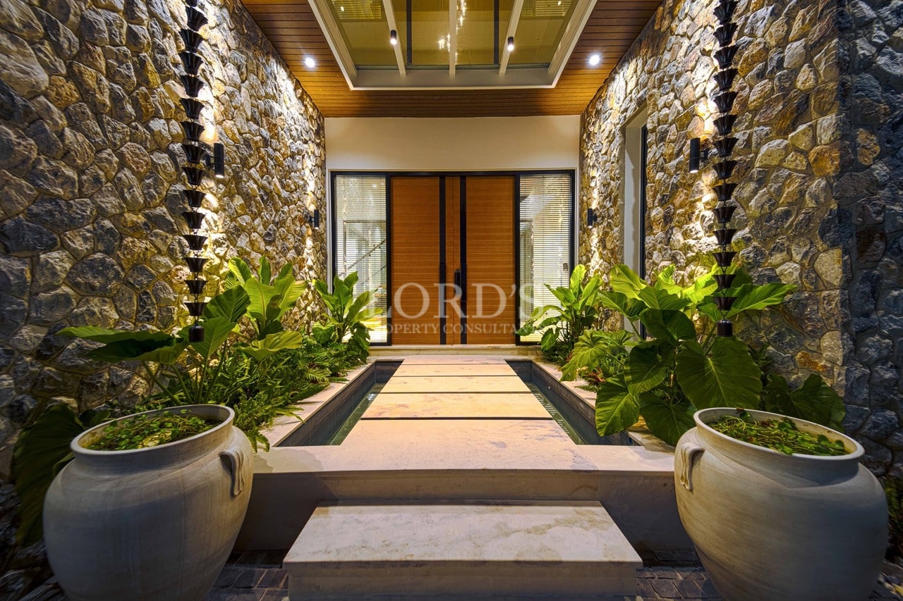 Eleganter, mit Stein verkleideter Villen-Eingang mit Wasserspiel und warmer Beleuchtung in der Nacht.