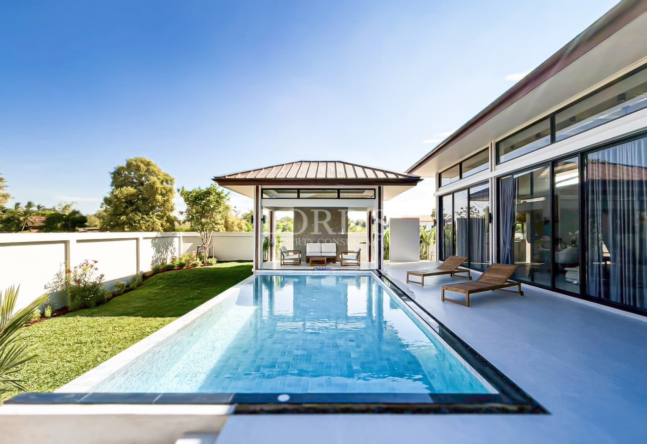 Modern luxury villa with private swimming pool, poolside loungers, and garden view under clear blue sky