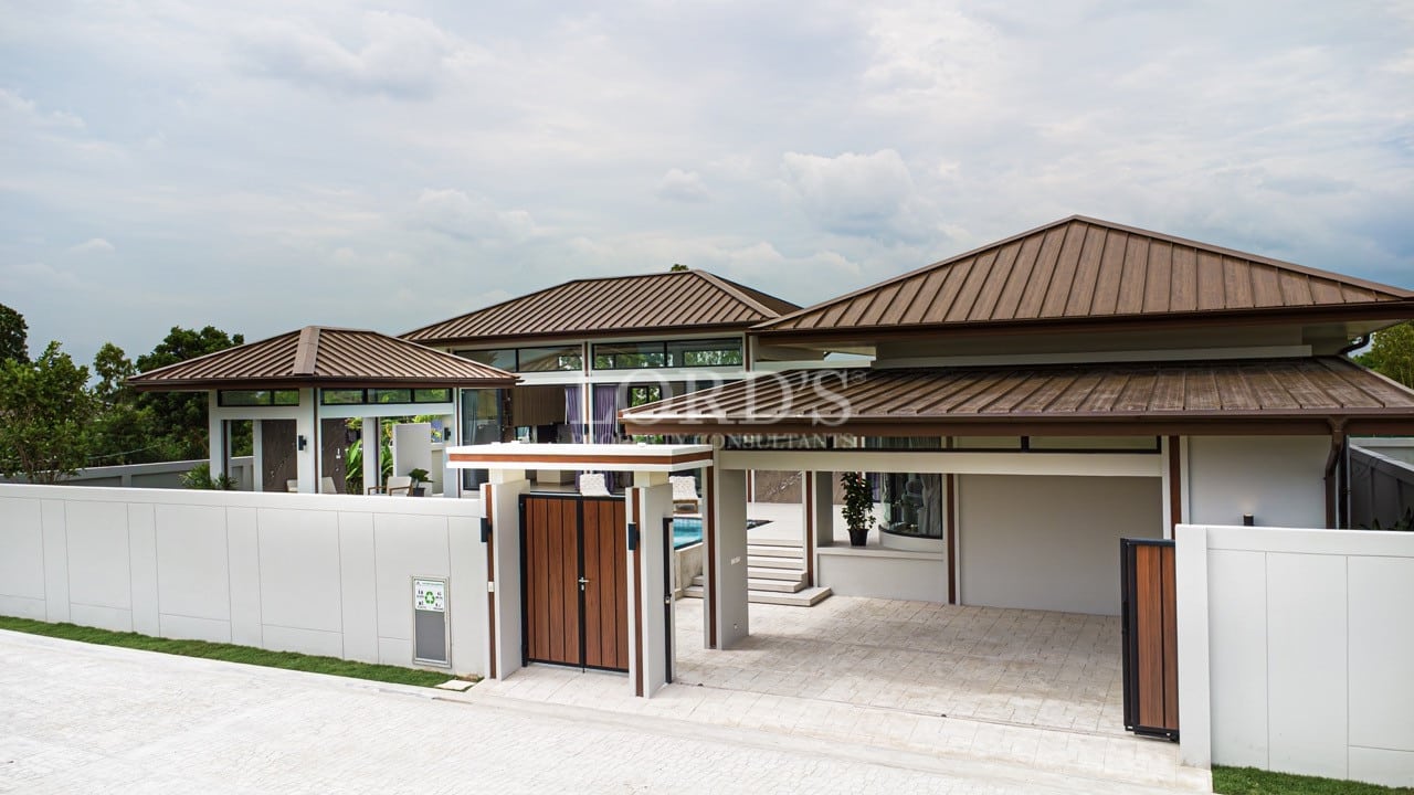 Modern luxury villa exterior with gated entrance, private driveway, and contemporary roof design.