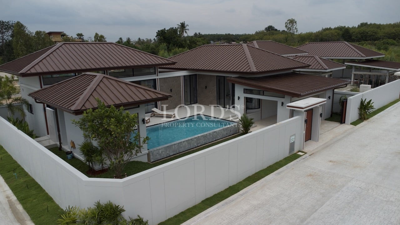 Aerial corner view of modern luxury villa with brown metal roofs, private pool, and high perimeter wall