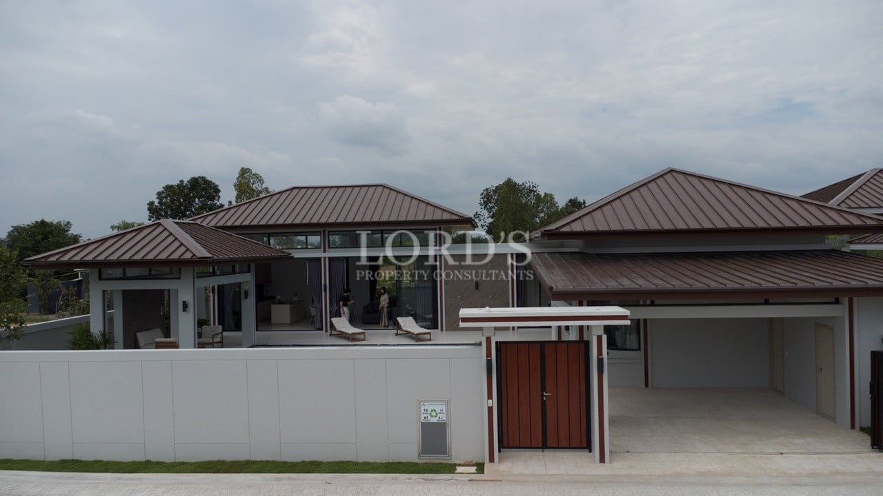 Front view of modern luxury villa with brown metal roofs, private gate, and covered carport