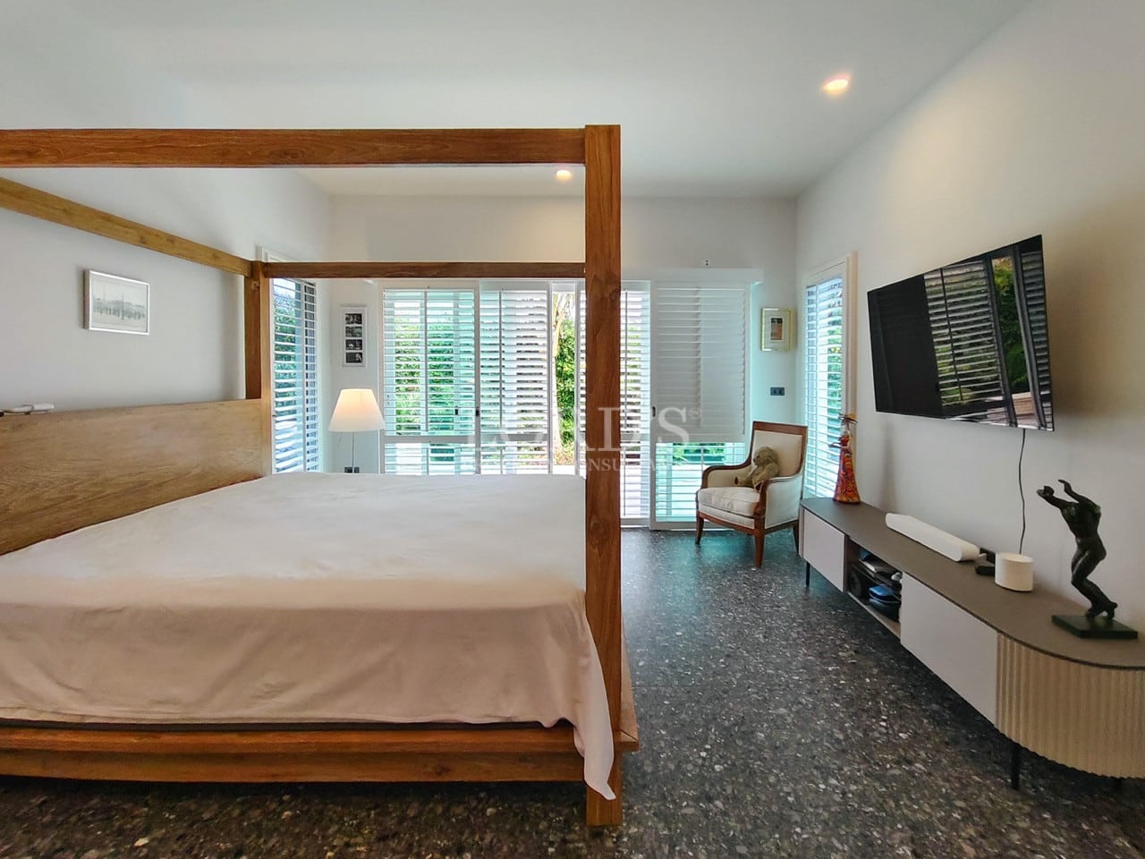 Spacious bedroom with wooden four-poster bed, wall-mounted TV, plantation shutters, and natural light.