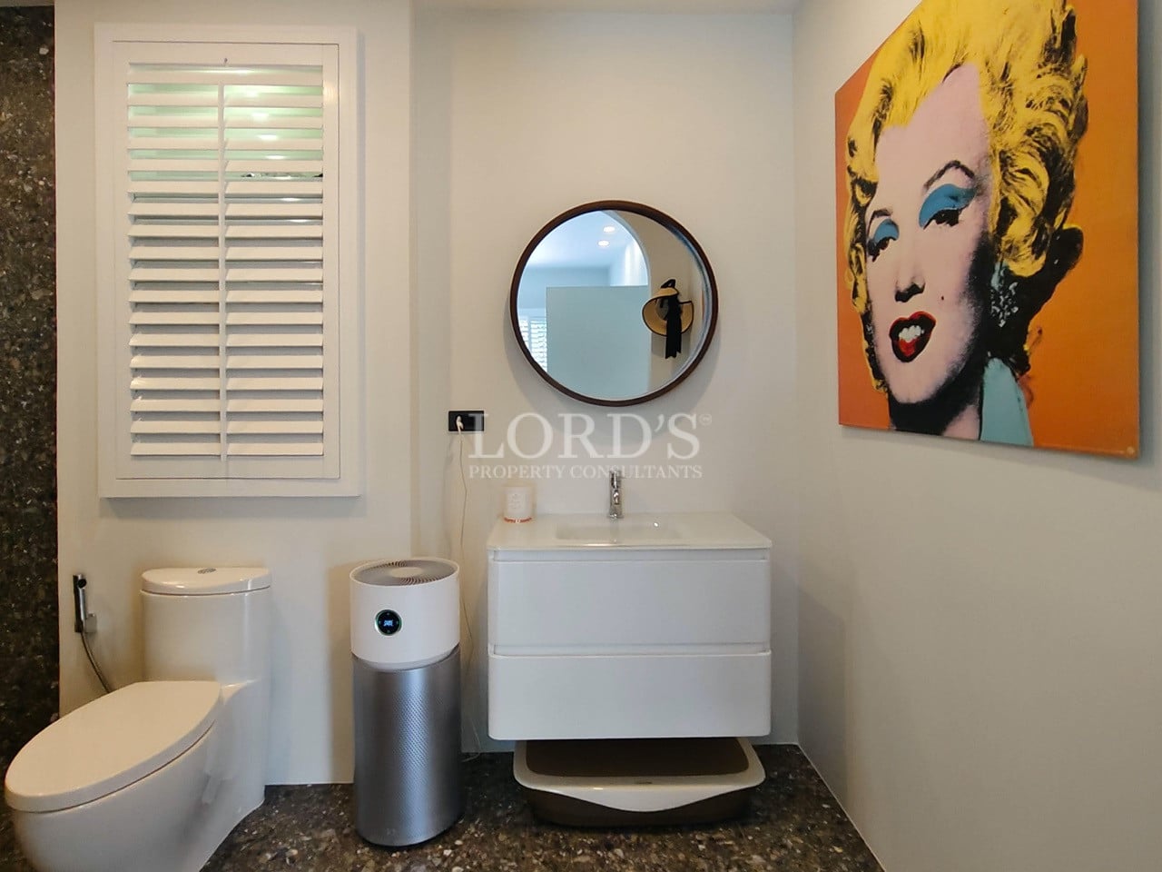 Modern bathroom vanity with round mirror, wall-mounted sink, toilet, and contemporary artwork.