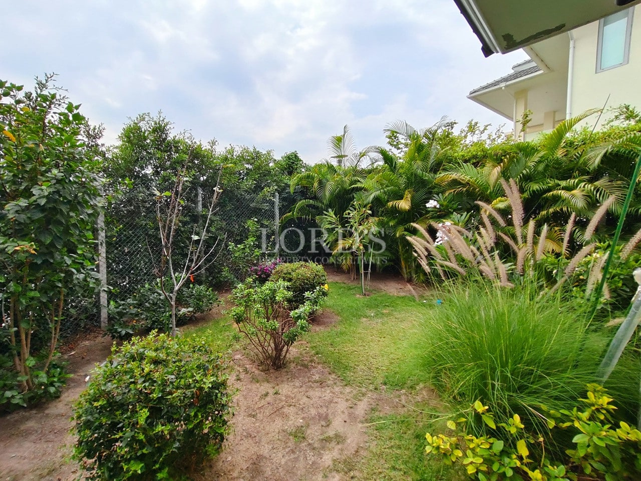 Private garden with lush greenery, manicured lawn, and tropical plants beside a modern villa.