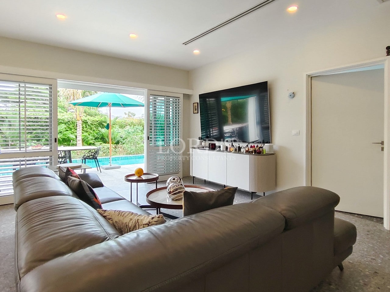 Bright modern living room with leather sofa, large TV, and sliding doors opening to a poolside terrace.