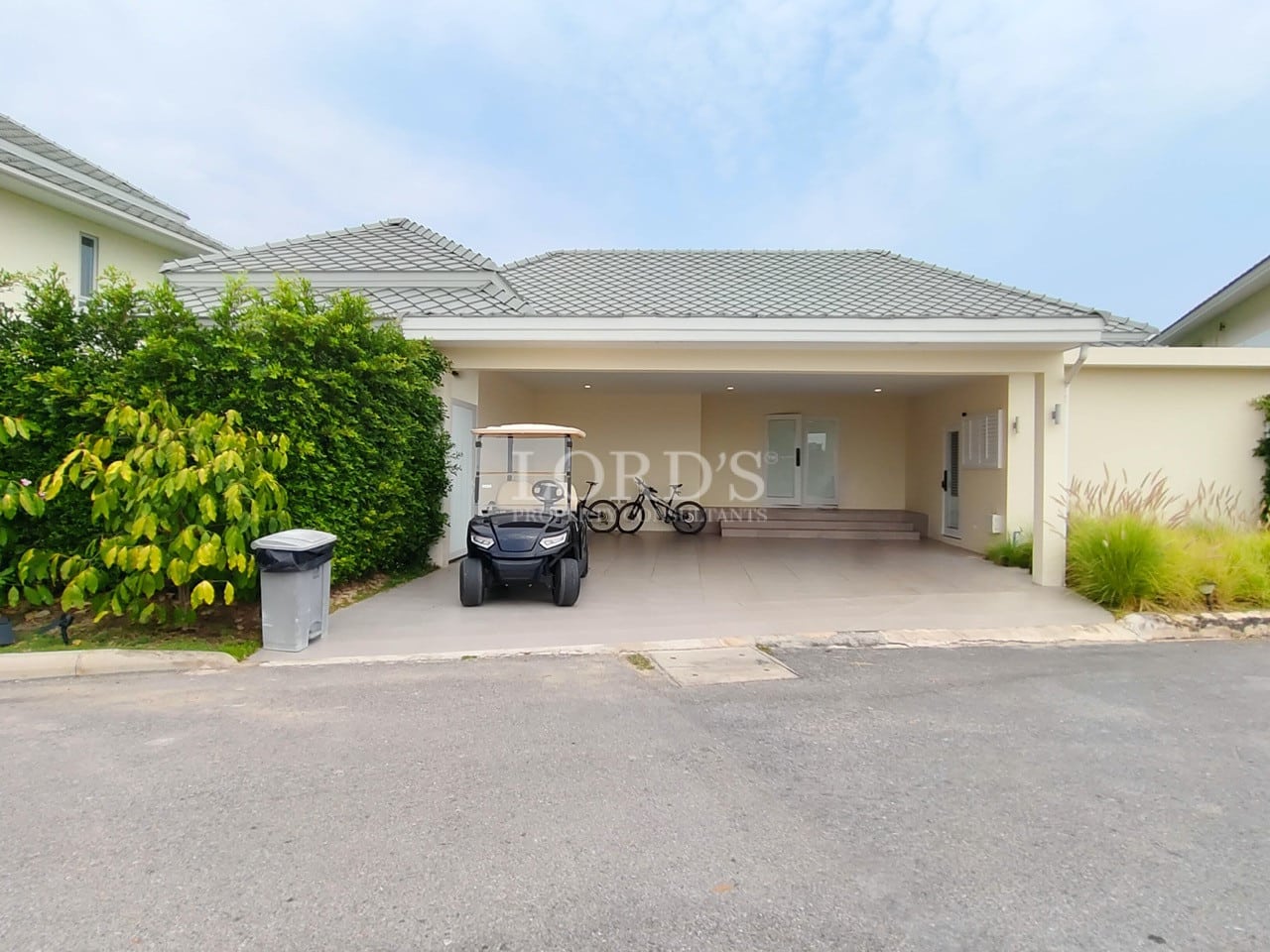 Covered parking area of a modern villa with driveway, bicycle storage, and landscaped greenery.