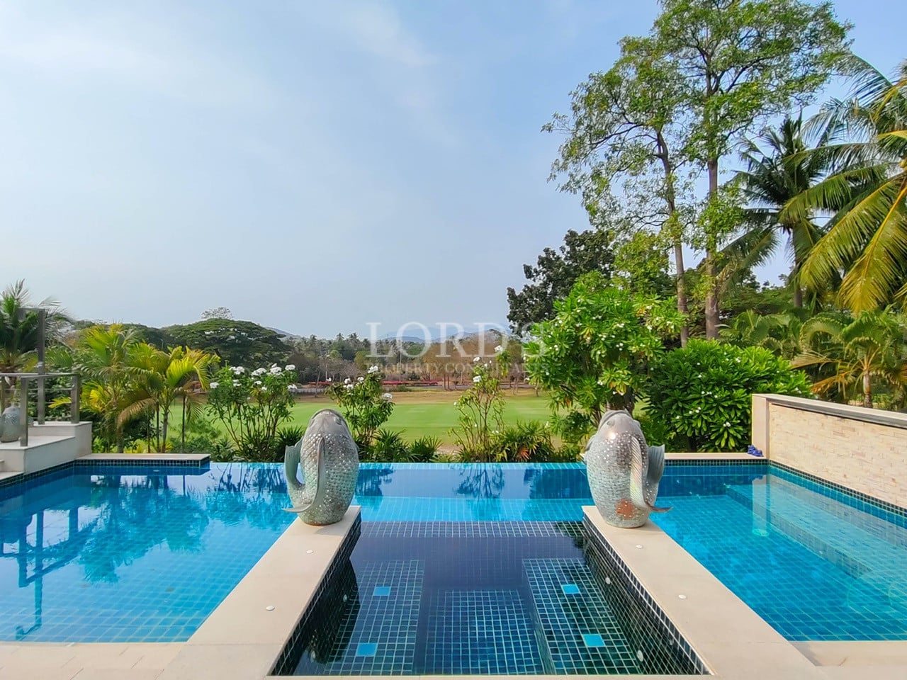 Infinity swimming pool with decorative sculptures overlooking green landscape and palm trees