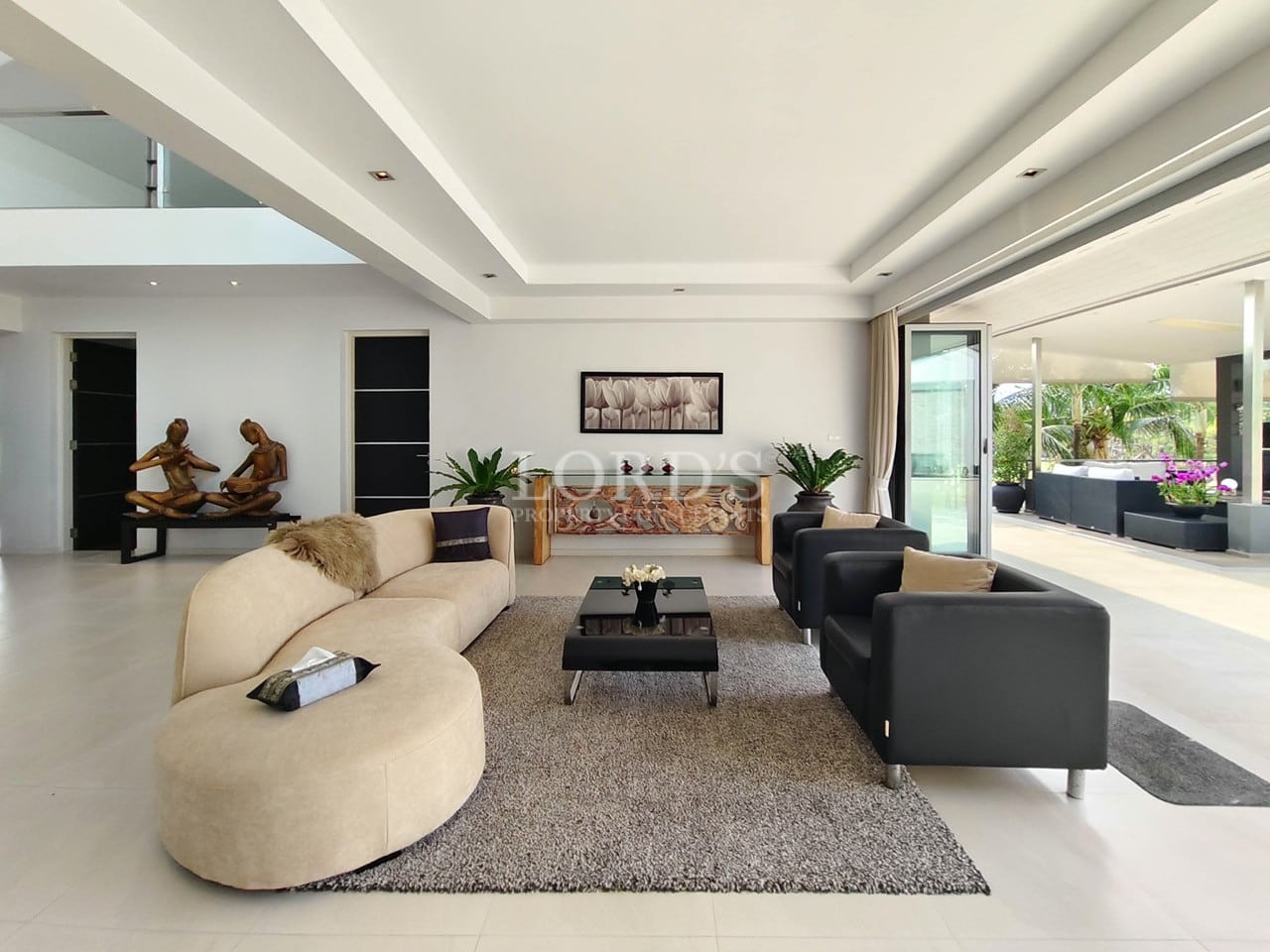 Modern luxury living room with beige curved sofa, black armchairs, and large sliding glass doors opening to a terrace