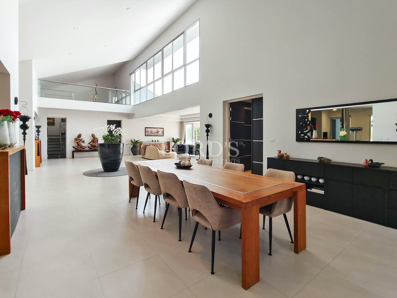 Open-plan luxury dining area with long wooden table and double-height ceiling.