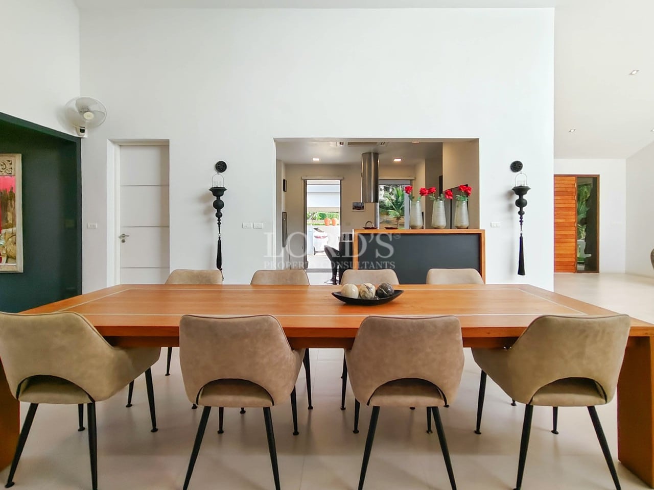 Modern dining area with wooden table, upholstered chairs, and open kitchen view.