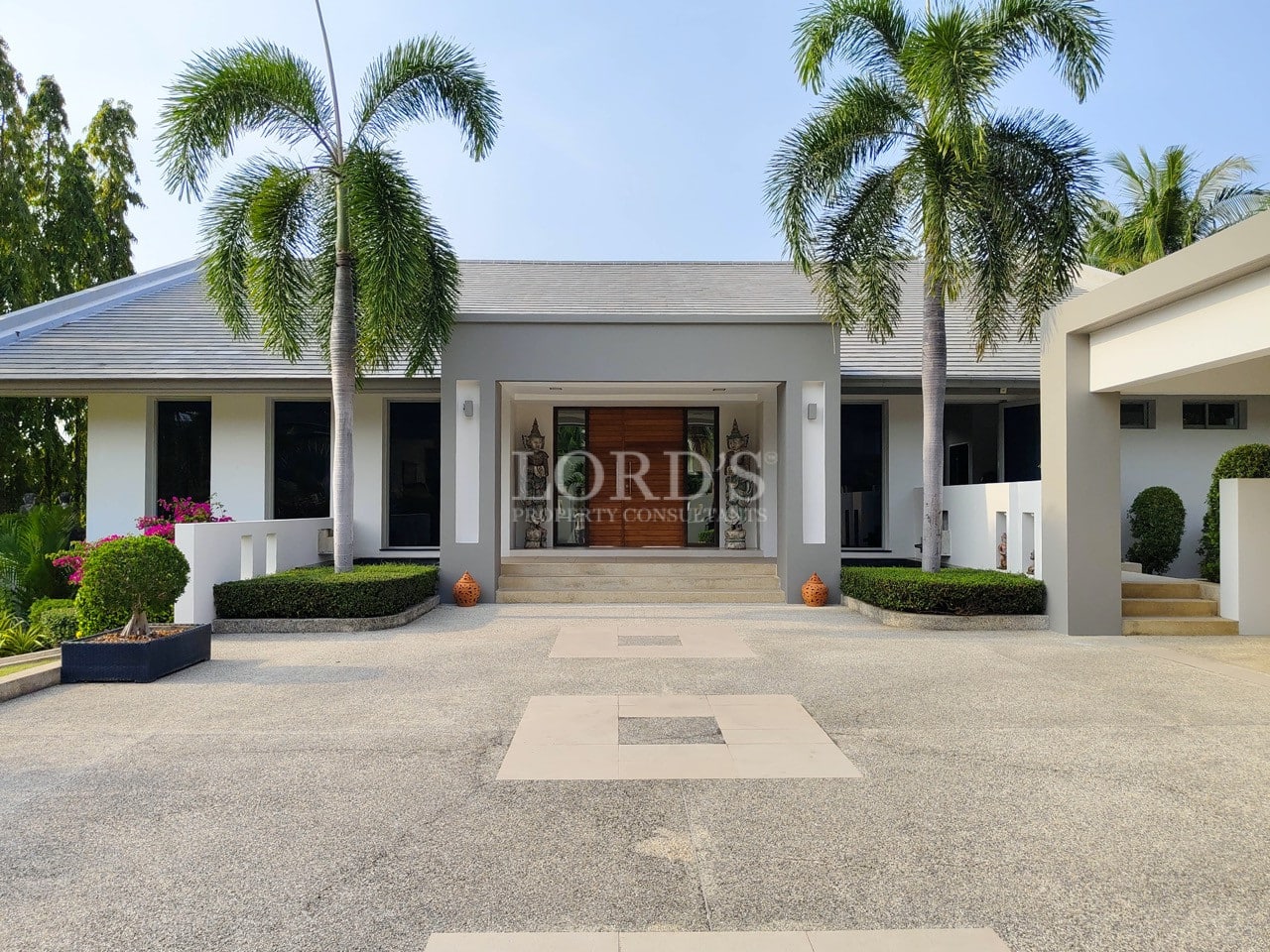 Front entrance of a modern luxury villa with palm trees and landscaped driveway.