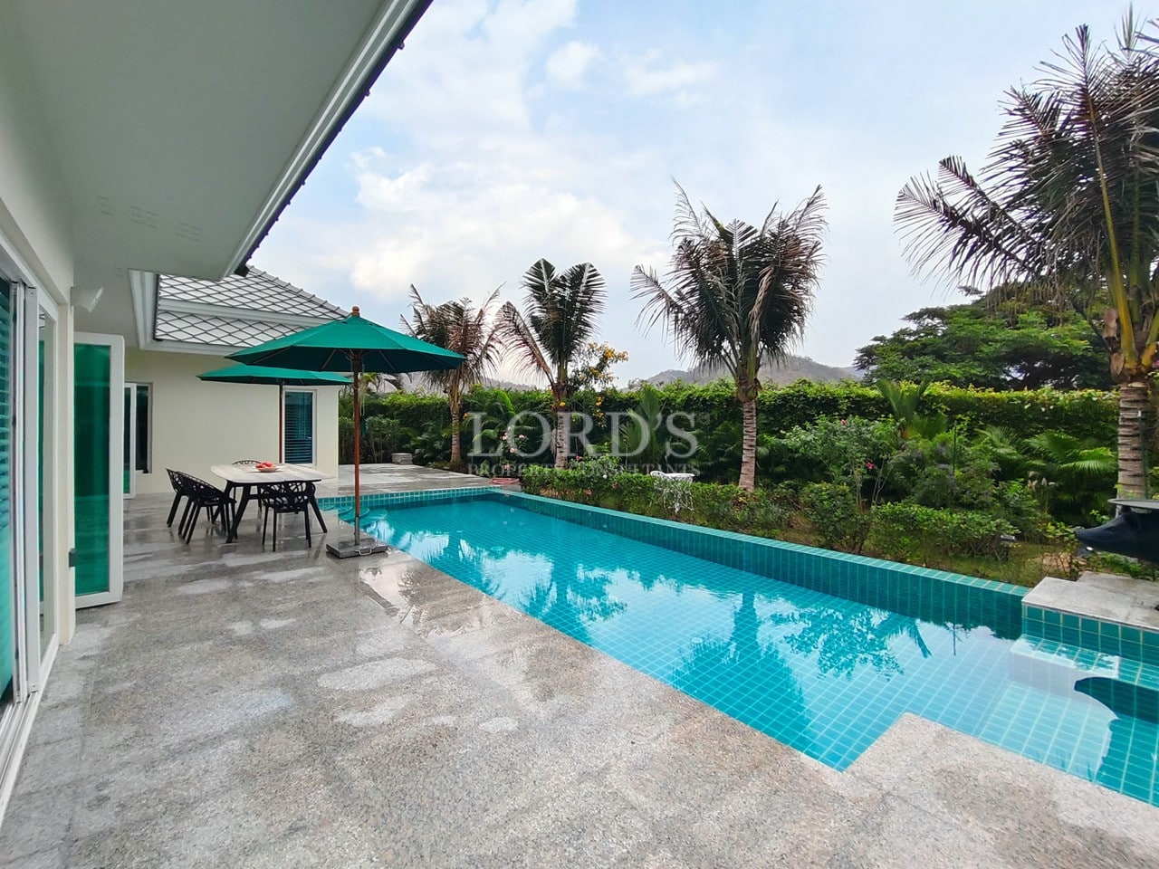 Modern private pool villa with outdoor dining area, palm trees, and landscaped tropical garden.