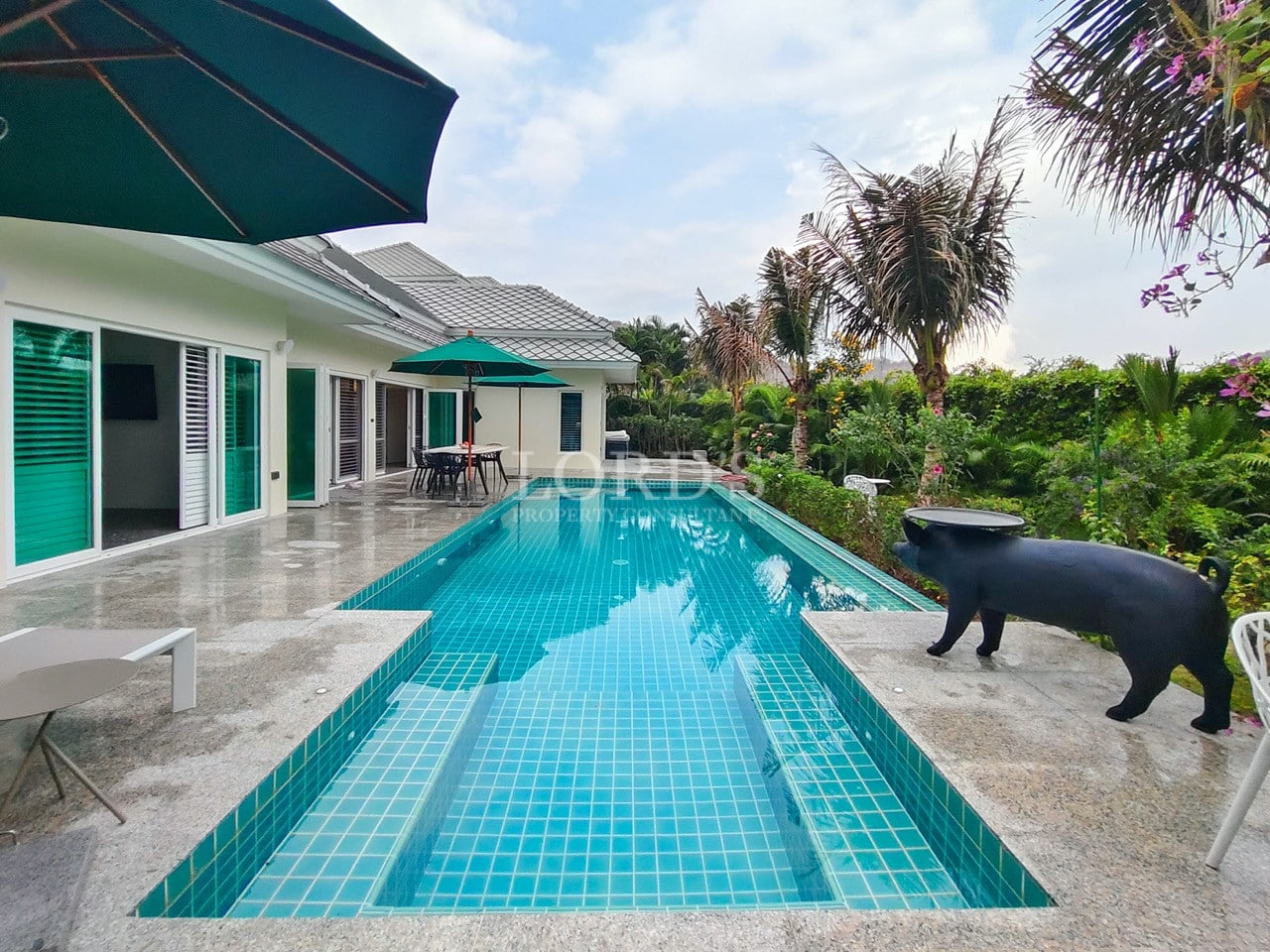 Private swimming pool beside a modern tropical villa with outdoor seating and lush garden views.
