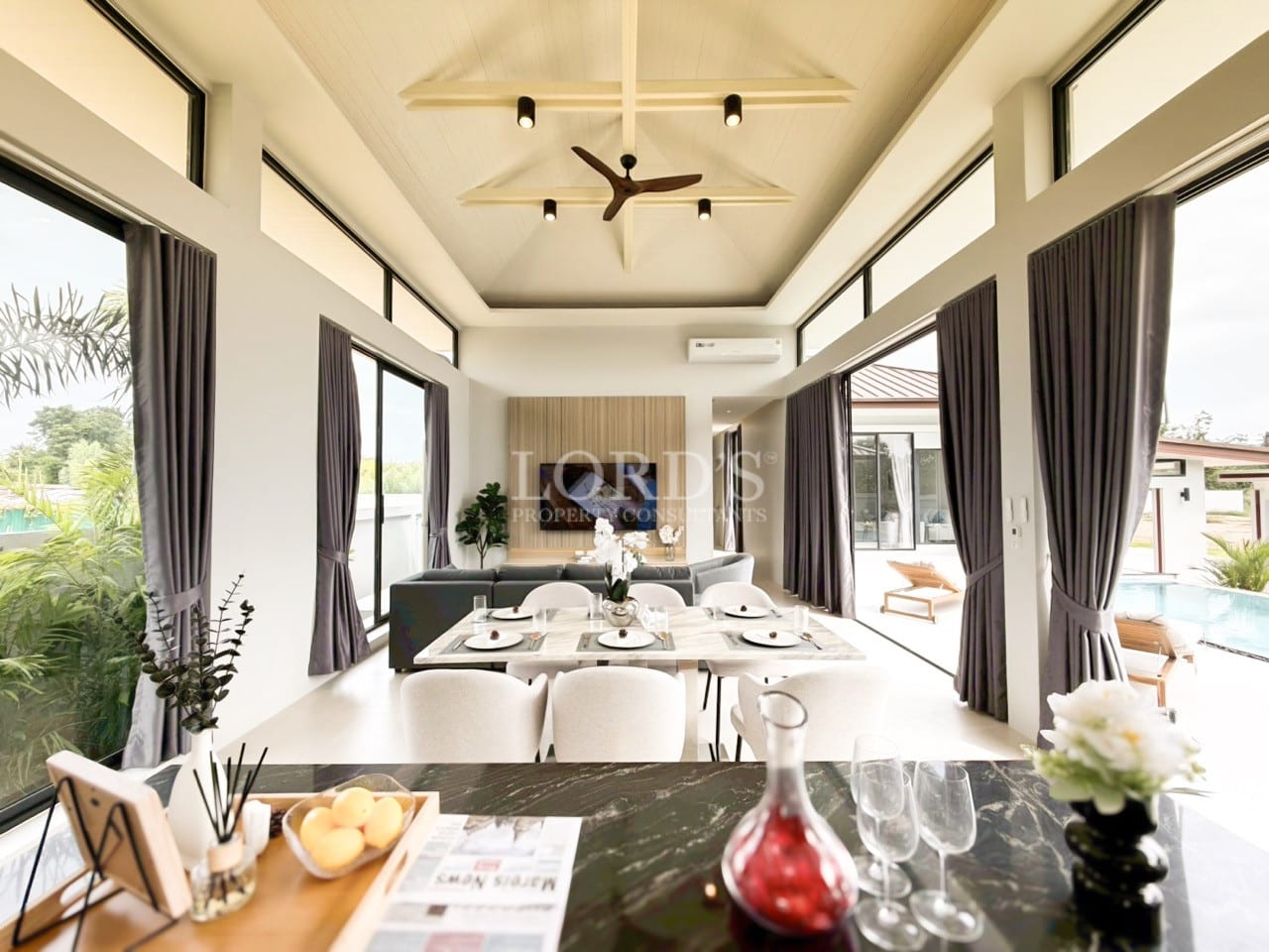 Modern open-plan living and dining area with high ceiling, large windows, and poolside view