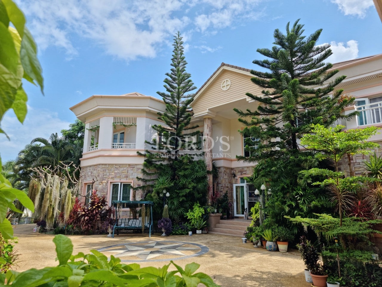 Luxury villa exterior with landscaped courtyard, tropical trees, and elegant two-story architecture.